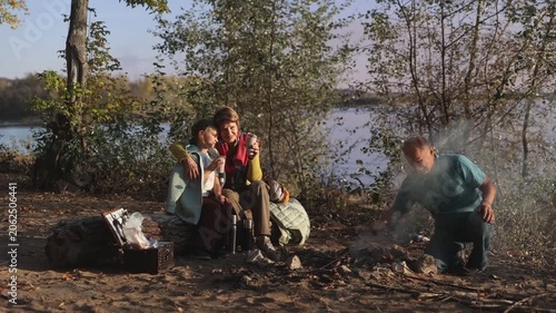 Little child girl with grandpa and grandmother Having a picnic on the beach on a sunny autumn day. Concept of friendly family.  Family  roasts marshmallows and sausages on the campfire.