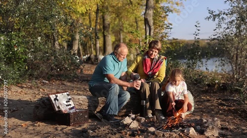 Little child girl with grandpa and grandmother Having a picnic on the beach on a sunny autumn day. Concept of friendly family.  Family  roasts marshmallows and sausages on the campfire.