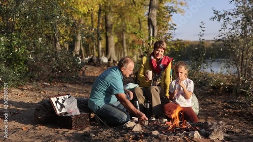 Little child girl with grandpa and grandmother Having a picnic on the beach on a sunny autumn day. Concept of friendly family.  Family  roasts marshmallows and sausages on the campfire.
