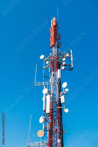 Cellular communication tower with multiple antennas and microwave dishes against clear blue sky, modern telecommunications infrastructure