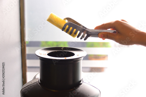 Fotografie a hand using a tong to pick up a piece of fresh pineapple into the fruit juice e