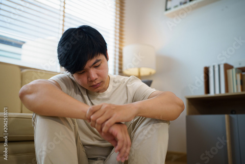 Depressed Young Asian Man Sitting Alone on Floor at Home Looking Down in Deep Thought