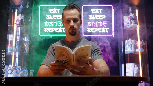 Man reading manga comic in cyberspace room with neon signs and merch showcases