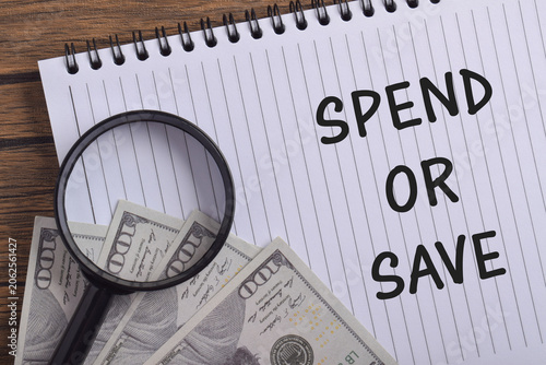 Принти на полотні Spend or Save text with cash, notebook and magnifying glass on a desk