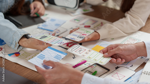 Foto Cropped hands of designers comparing mobile app paper wireframes for UX UI proto