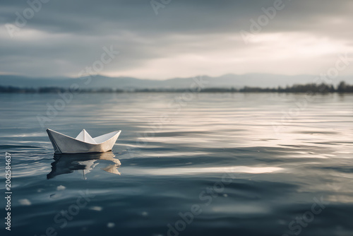 A delicate paper boat floats peacefully on still water, reflecting an overcast sky. A serene scene of solitude and gentle journey.