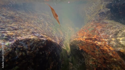 Underwater view of crystal clear freshwater flowing through a narrow granite crevice at Na Muang Waterfall 2 on Koh Samui, Thailand.