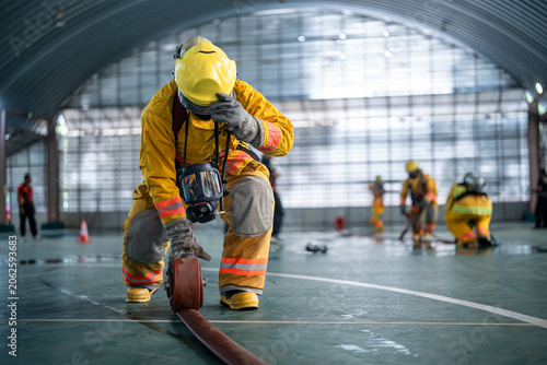 Professional firefighters wearing yellow protective suits practicing fire hose management during emergency response training inside a building