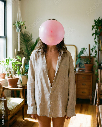 Anonymität und Identität: Kreatives Porträt einer Frau mit rosa Ballon vor dem Gesicht im hellen Zimmer.