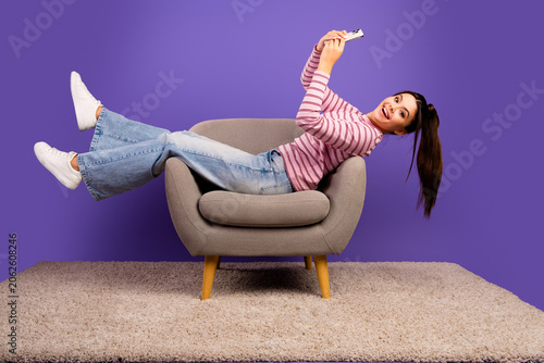 Принти на полотні Young woman smiling and reclining on a modern armchair while taking a selfie wit