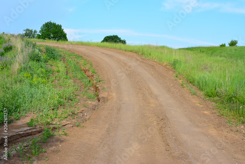 Dirt road winding uphill through green hills under a blue sky 