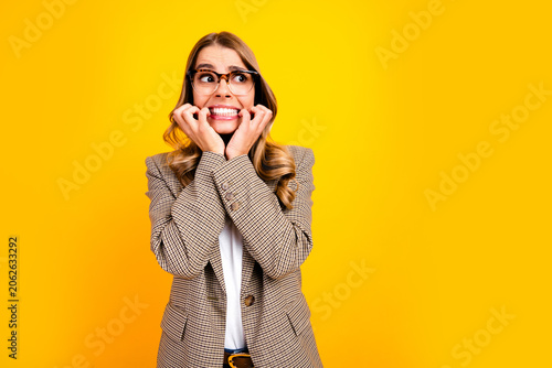 Slika na platnu Nervous young businesswoman in glasses wearing a checked blazer biting her nails