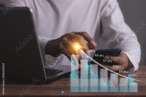 Young man with computer notebook and smartphone hand touching to visualize money growth The phone screen displays graphs and charts showing increasing investment and savings trends, increased account
