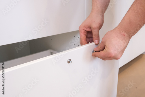 Installer attaching white cabinet drawer front with screws