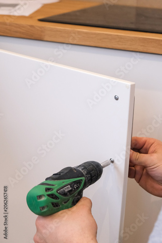 Person using cordless drill to attach white cabinet door in kitchen