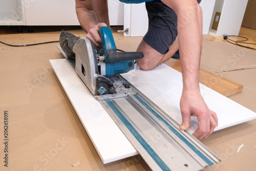 Person cutting a white board with a circular saw and guide rail