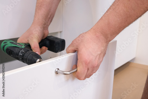Man installing metal handle on white kitchen drawer
