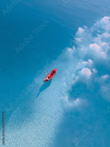 Red Kayak Drifting on Tranquil Blue Water: An aerial view captures a single red kayak gently floating on a vast expanse of clear, calm blue water, with fluffy white clouds drifting above.