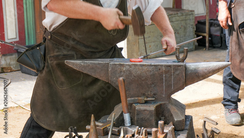 Photos traditional blacksmith using a heavy hammer to forge hot glowing metal on a stee