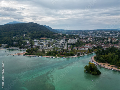 Aerial Drone View of Lake Annecy Waterfront Peninsula, Marina with Boats, and City of Annecy Surrounded by Green Hills and Forest Under Cloudy Sky, Haute‑Savoie, French Alps, France
