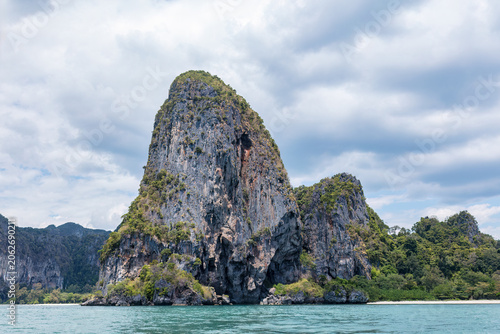 Limestone cliff and coastline at Railay Beach in Krabi, southern Thailand. Blue waters of the Andaman Sea in the foreground; cloudy sky above. 
