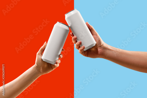 Fotografie Blank aluminum cans held by two hands in a toast gesture over split red and blue background