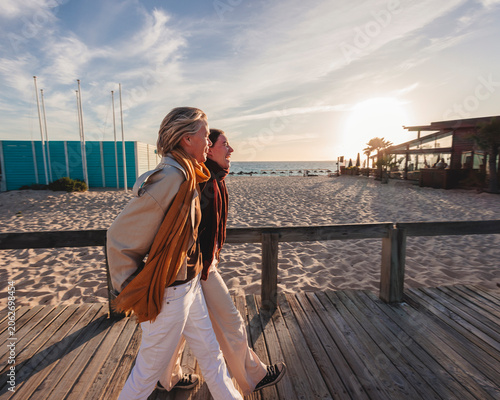 Cuadro en lienzo Women walking on beach boardwalk during sunset with scarf in motion adding a rel