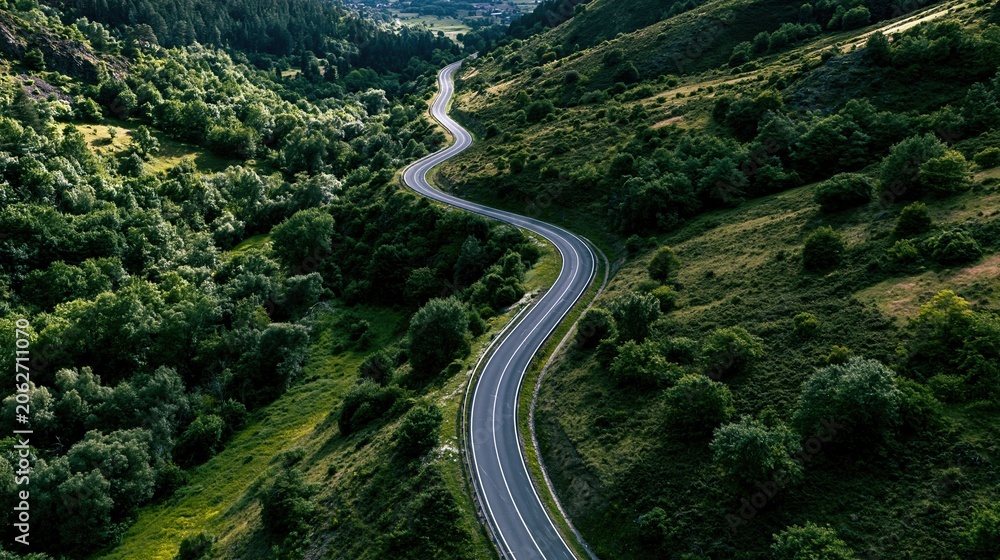 Fototapeta premium Scenic winding road through lush green forested mountain valley, offering breathtaking aerial views of nature's beauty