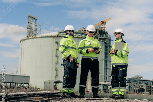 Energy plant maintenance engineers collaborate at refinery industrial site safety procedures outdoors professionalism