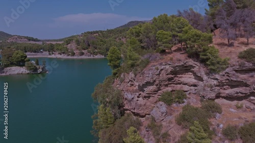Drone footage ascending over El Chorro's secluded inlet, lifting past pine treetops to reveal an emerald cove, sandy shoreline, forested hillside, and limestone peaks beyond.