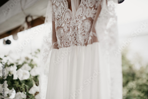 Photos Close up of an elegant white wedding dress with detailed lace bodice hanging outdoors