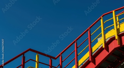 Modern industrial staircase featuring bright red and yellow metal railings, sharply contrasting the deep blue backdrop of the clear sky, red, stairs, vertical