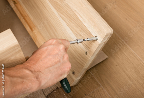 Obraz na plátně Hand tightening a screwdriver on wooden furniture assembly