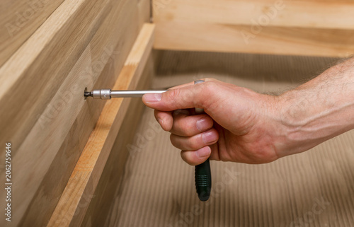 Fotografie Hand tightening a screw in wooden furniture