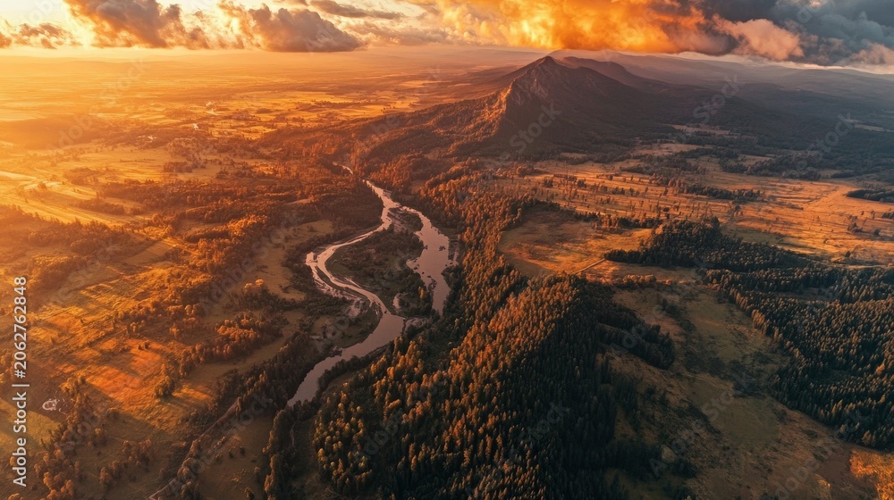 Fototapeta premium Aerial drone view of a winding river flowing through a vast mountain valley at sunset with clouds