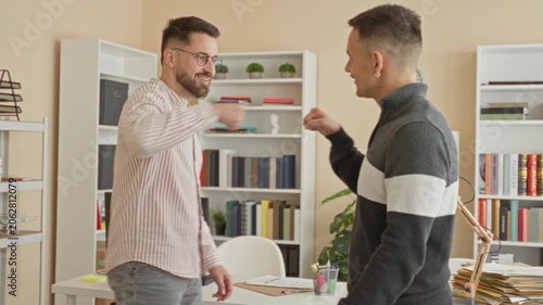 Man extending hand for handshake and occasional fist bump across cluttered desk with papers, lamp and bookshelves in office building; friendly teamwork.