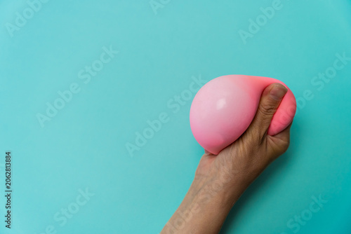 Photos Hand squeezing a pink anti-stress dumpling toy against a light blue background,