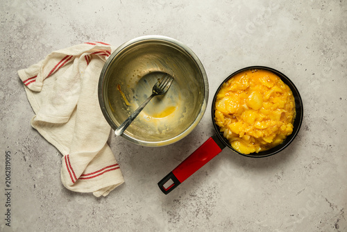 Bol y sartén con huevo y patatas para preparar una tortilla, sobre un fondo gris claro con textura de cemento.