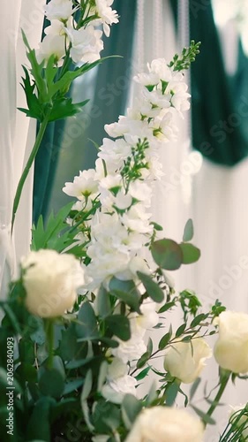 A romantic wedding arch made of white roses and green tulle before the bride and groom ceremony. Decor and floristry