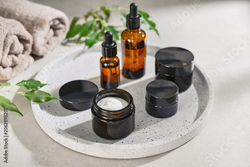 Natural skincare and beauty treatment concept with amber glass cosmetic containers arranged on a round tray.