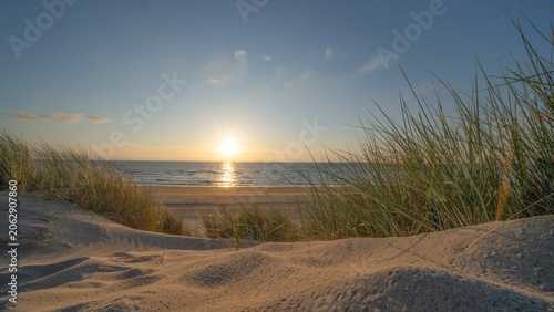 Panoramic landscape background banner panorama of sand dune, beach and ocean North Sea with blue sky, clouds and sunbeams sunset