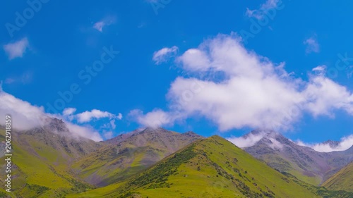 Zooming in time-lapse of green mountains in Kyrgyzstan at sunny summer day with white clouds flowing above