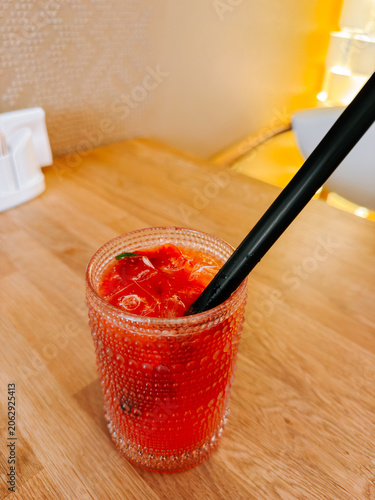 Refreshing red beverage with ice and a black straw on a wooden table indoors