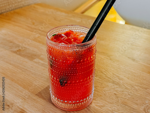 Refreshing red berry drink with ice and a black straw on a wooden table
