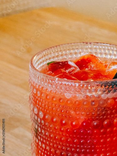 Cool red beverage with ice cubes in a textured glass on a wooden table