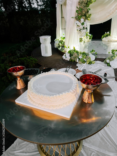 Elegant white cake with fresh berries set on a gold table at an outdoor evening celebration