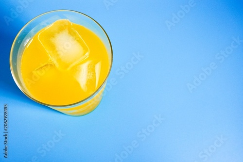 Fotografie Yellow mango juice in transparent glass isolated on horizontal blue colored background from top angle view