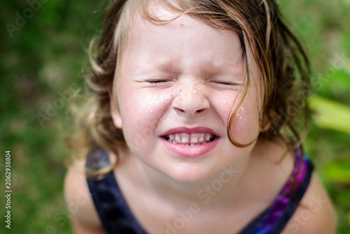 summer portrait of a cute little girl in close-up. The child smiles at the camera. A little girl with blonde hair makes faces