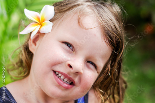 summer portrait of a cute little girl in close-up. The child smiles at the camera. A little girl with blonde hair makes faces