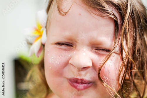 summer portrait of a cute little girl in close-up. The child smiles at the camera. A little girl with blonde hair makes faces